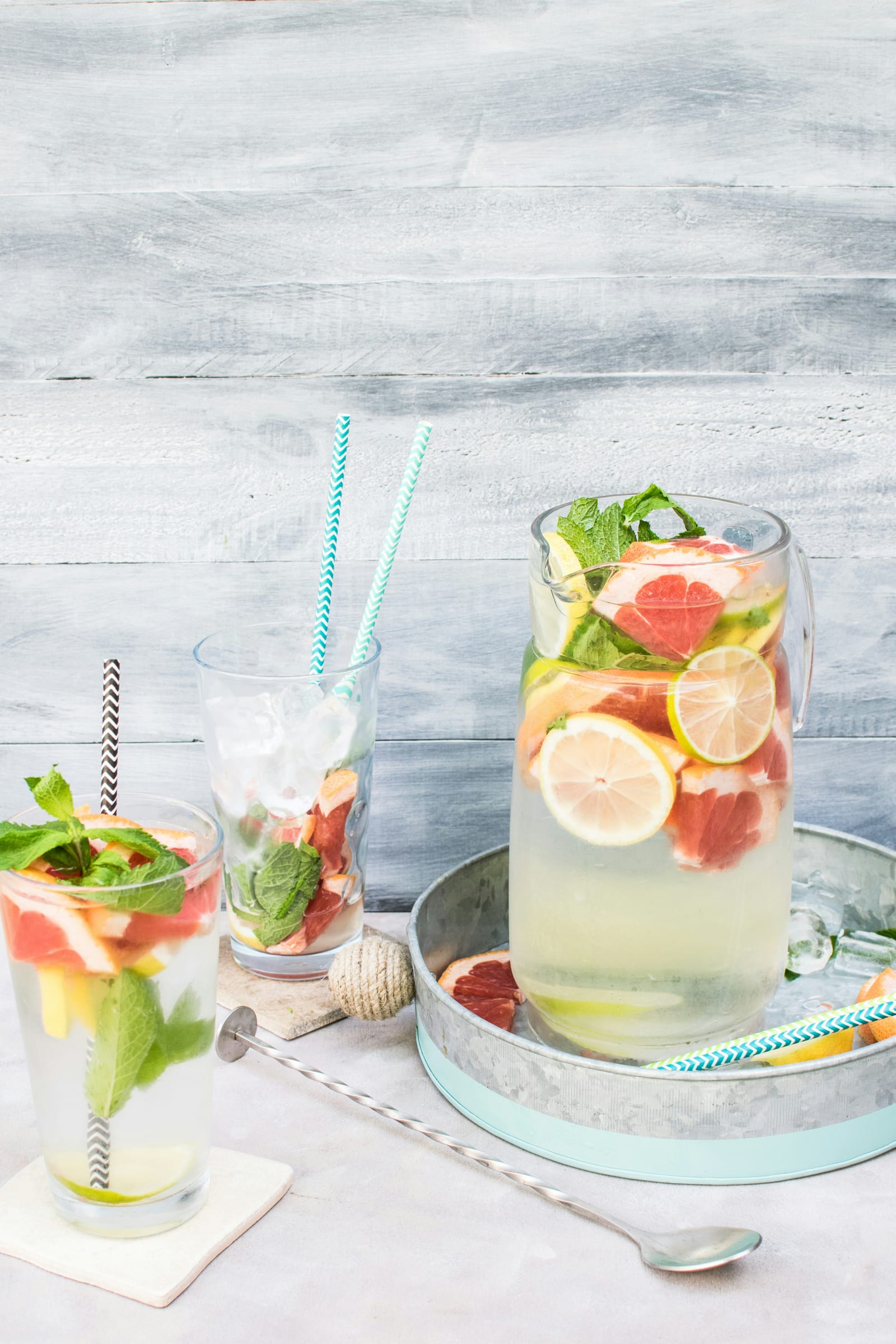 Grapefruit, lemon, lime and mint infused water in glasses and a pitcher on a galvanized tray