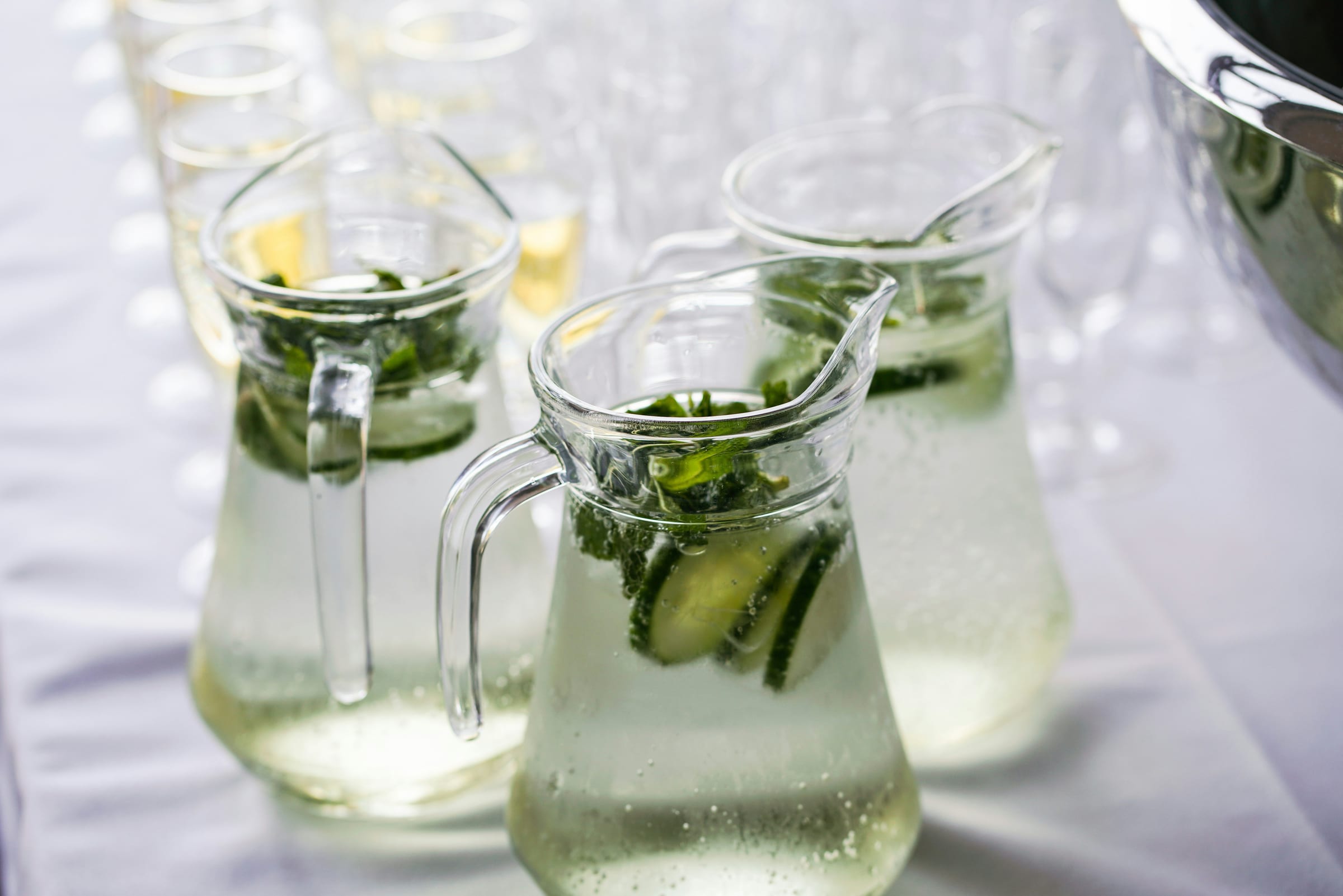 Clear glass pitchers of cucumber-and-mint infused water on a white tablecloth