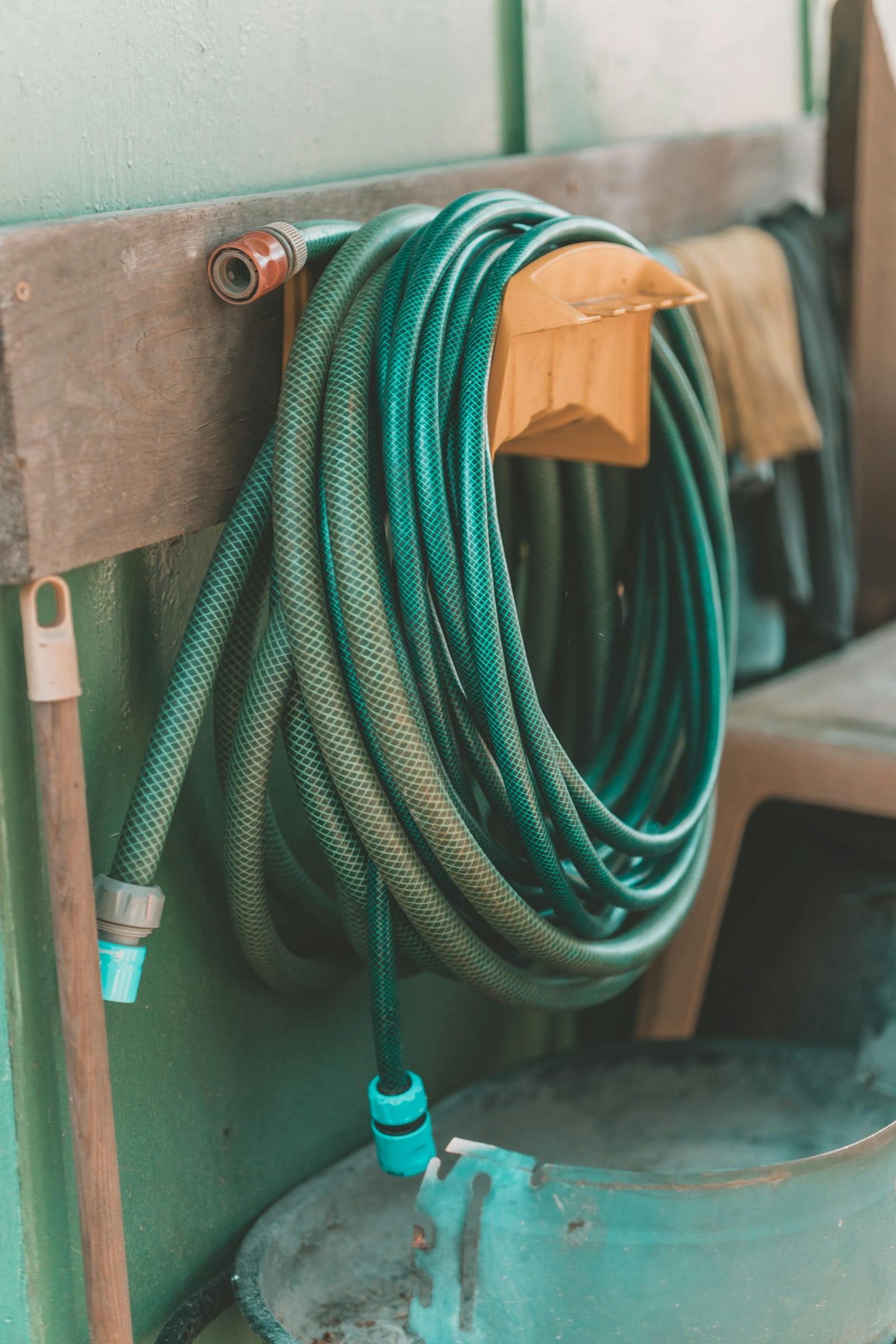 A green garden hose coiled on an orange wall holder next to a spigot on a weathered wood wall