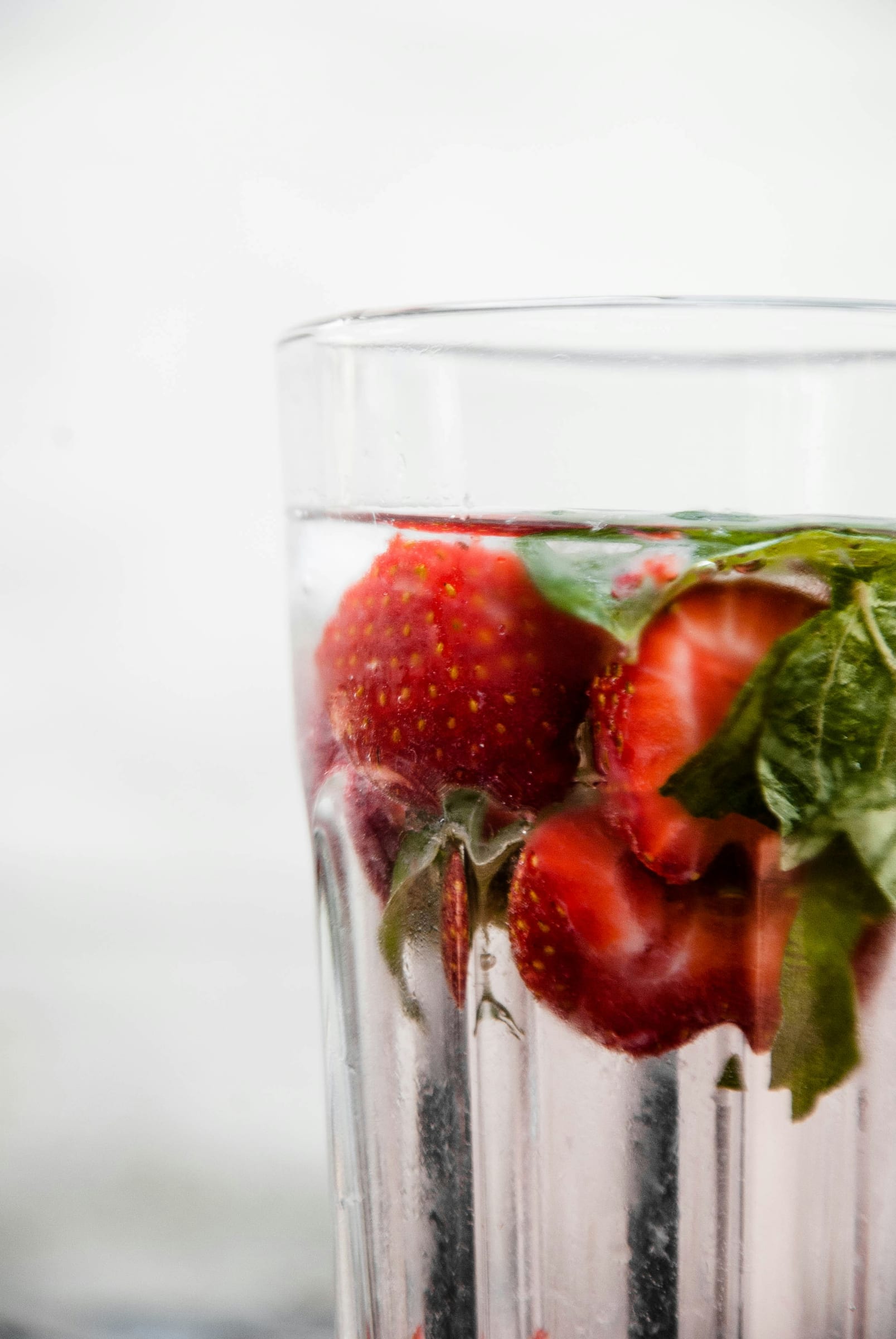 A close-up of a tall glass of strawberry-infused water with fresh strawberries and mint leaves