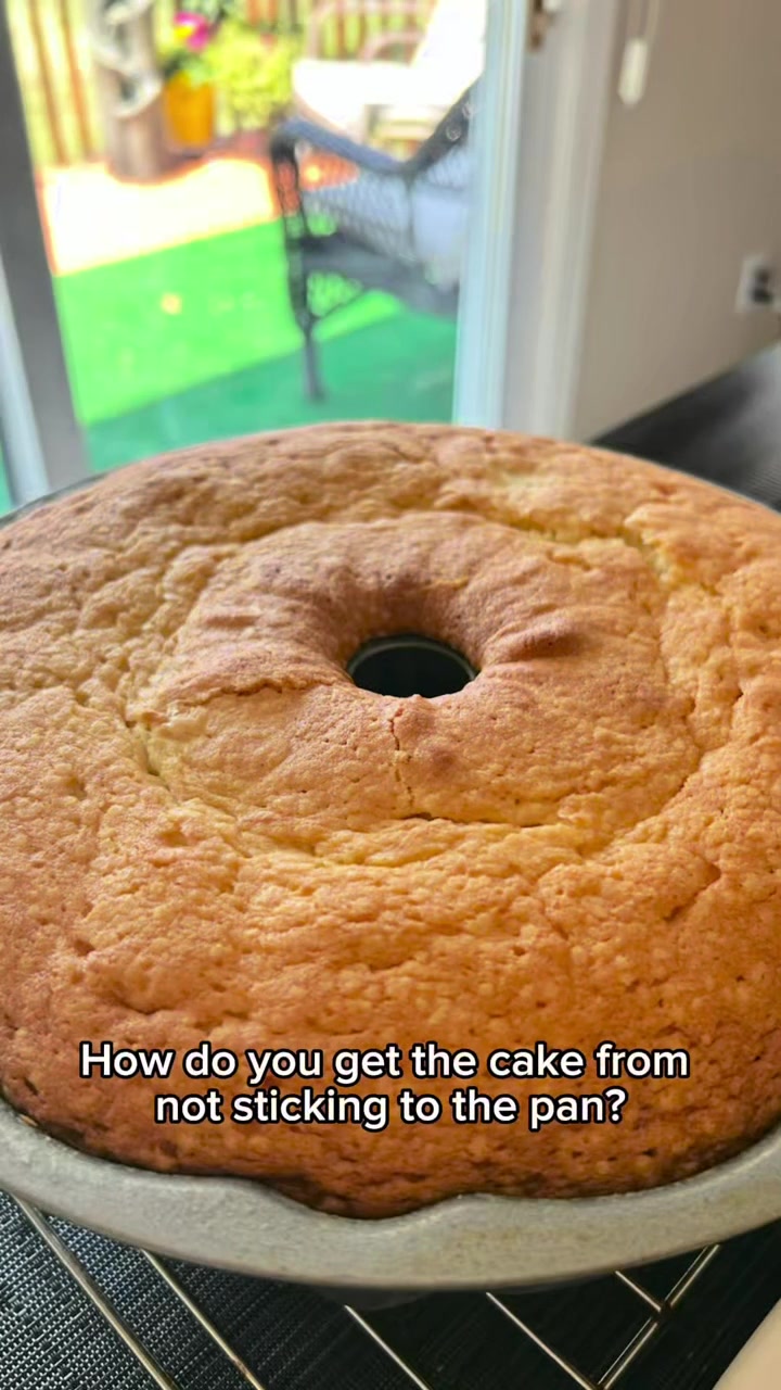 A golden pound cake resting in its bundt pan on a cooling rack by a sunny kitchen window