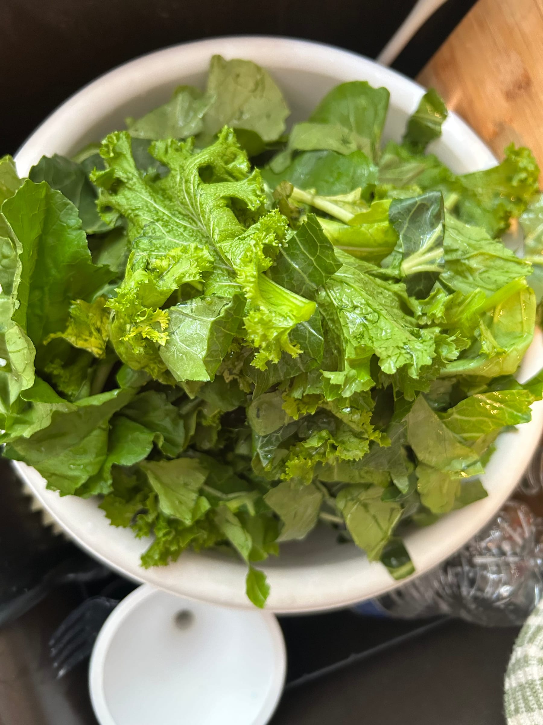 A white pedestal bowl heaped with freshly washed mustard and turnip greens