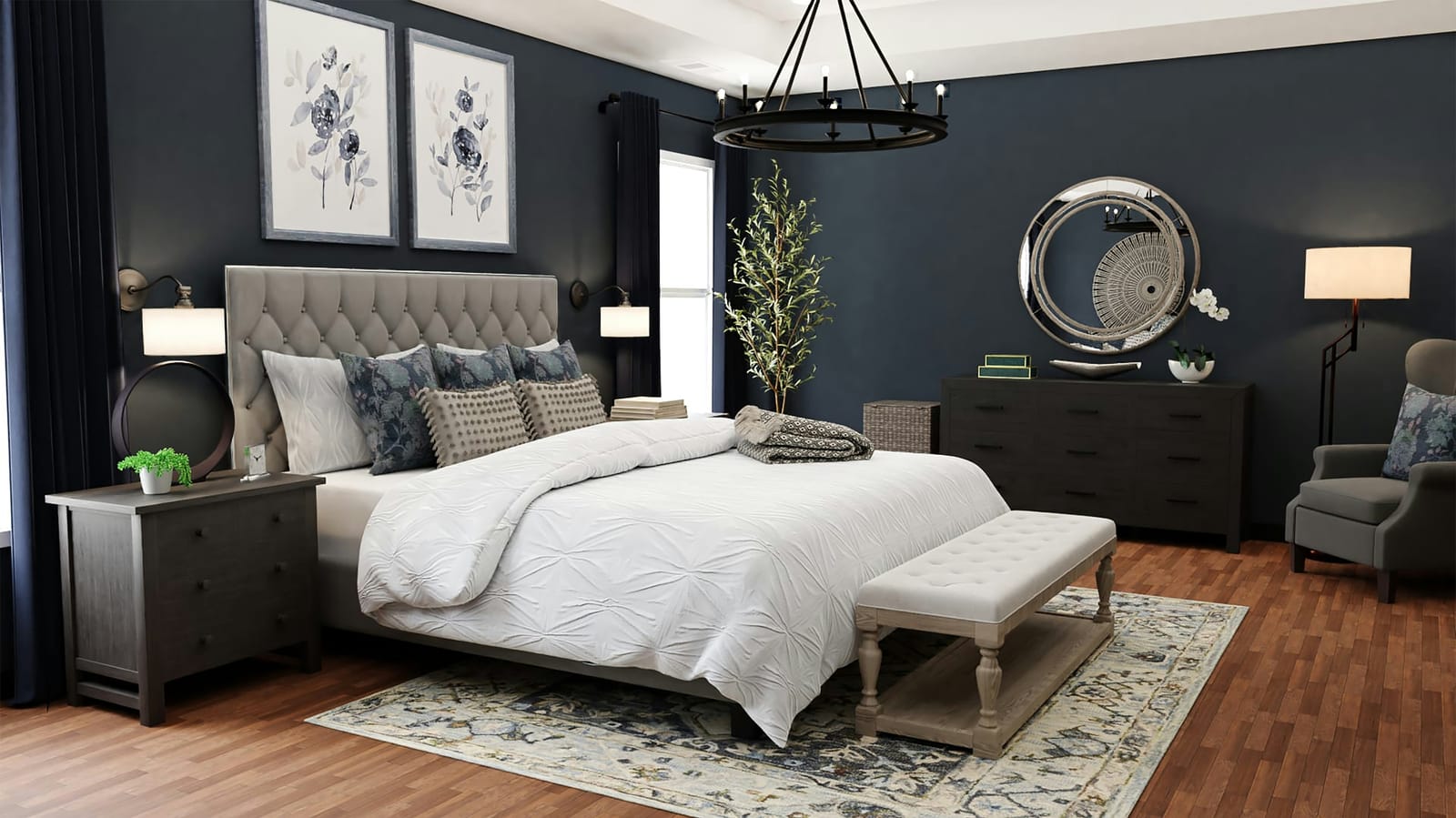 A moody navy-blue bedroom with a gray tufted headboard, white pintuck bedding, floral watercolor prints, a black wagon-wheel chandelier, and an olive tree