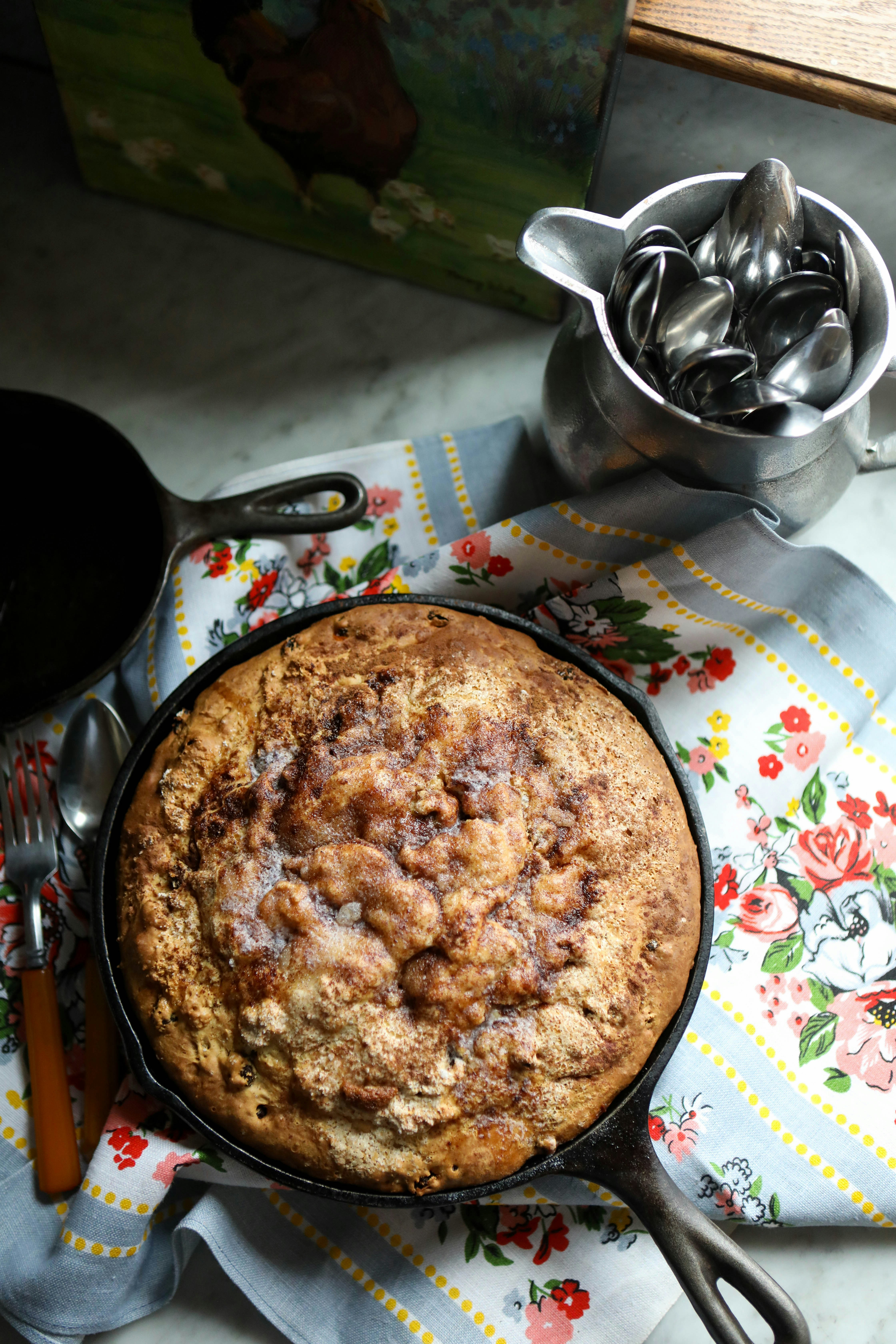 An overhead cinnamon-sugar apple skillet cake in a cast iron pan on a vintage floral tea towel