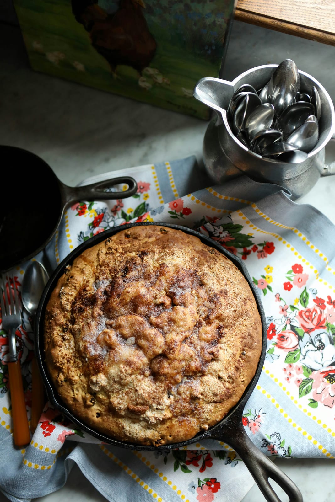 An overhead cinnamon-sugar apple skillet cake in a cast iron pan on a vintage floral tea towel