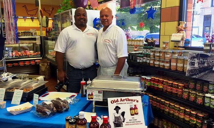 Two generations of the Old Arthur’s family behind a table stocked with their barbecue sauces at a storefront event