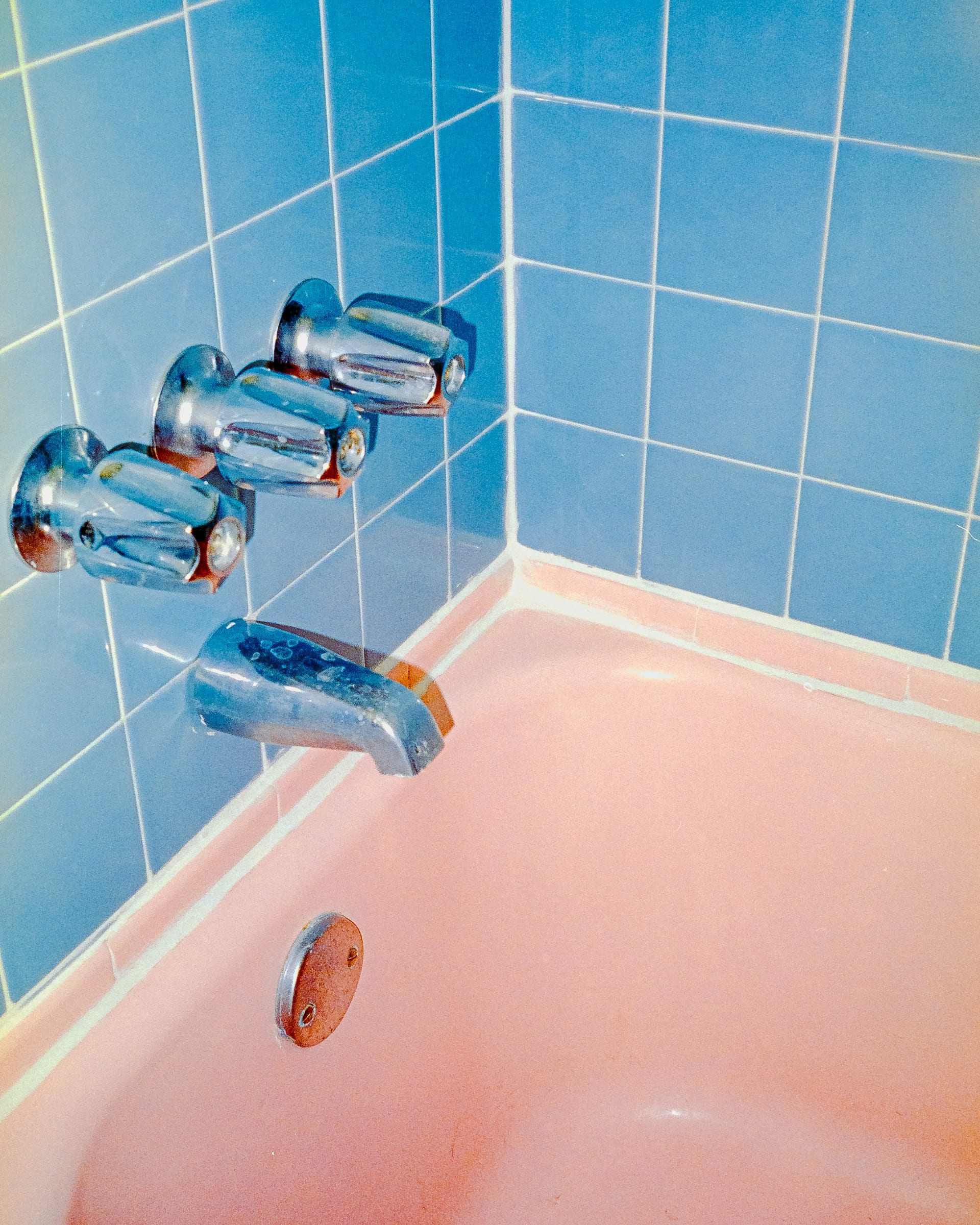 A vintage bathroom with a salmon-pink bathtub, powder-blue tile and chrome faucet handles